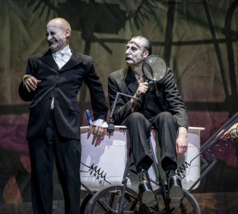 Od lewej Wiktor Frankenstein (Kiljan), monstrum (Studniak) i Igor (Picher). Monstrum siedzi na wózku laboratoryjnym, trzyma szkło powiększające. Wiktor oparty o wózek plecami, krzywi twarz. Obydwoje patrzą w jednym kierunku. Igor wychodzi z kadru z prawej strony.