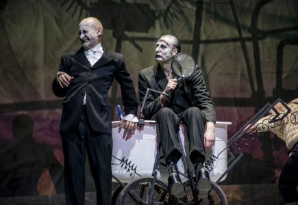 Od lewej Wiktor Frankenstein (Kiljan), monstrum (Studniak) i Igor (Picher). Monstrum siedzi na wózku laboratoryjnym, trzyma szkło powiększające. Wiktor oparty o wózek plecami, krzywi twarz. Obydwoje patrzą w jednym kierunku. Igor wychodzi z kadru z prawej strony.