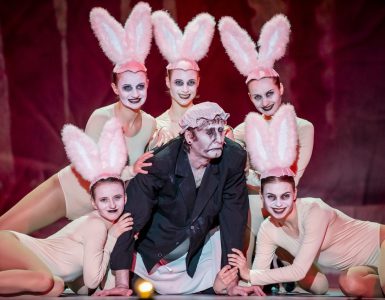 W centrum Monstrum (Cezary Studniak). Ma na sobie czarną marynarkę i kobiecy czepek na głowie. Otacza go grupa tancerek – zajączków. Monstrum ma zamknięte oczy i usta. Z kolei kobiety wpatrują się w widownię, uśmiechając się szeroko.