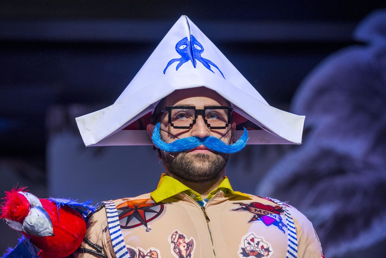 Zbliżenie na twarz Pirata, mężczyzny w okularach, który w innych scenach jest Drzewem, Księżycem, Tatą, Olbrzymem. Ma na głowie trójkątną czapkę z ośmiornicą, imitacje tatuaży na cielistym kostiumie, sumiaste niebieskie wąsy, na jego prawym ramieniu siedzi kolorowa, zabawkowa papuga.