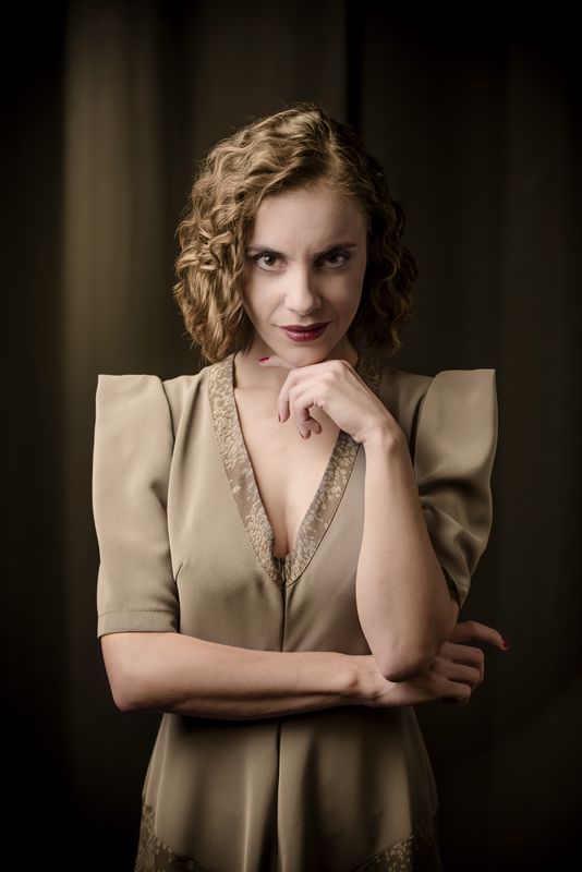 Portret Justyny Antoniak, kreującej rolę Małgorzaty. Ubrana w oliwkową sukienkę z dekoltem karo, jest szatynką, ma półdługie, falujące włosy, bez grzywki. Patrzy wprost, lekko się uśmiecha. Kolorystyka beżu i sepii, z zaznaczoną czerwienią uszminkowanych ust i lakieru na paznokciach.